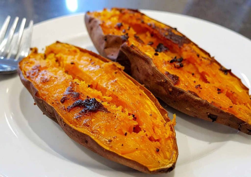 Is Sweet Potato Good for Weight Loss? 12 1. Two baked sweet potatoes arranged on a white plate, showcasing their golden-brown skin and soft interior.