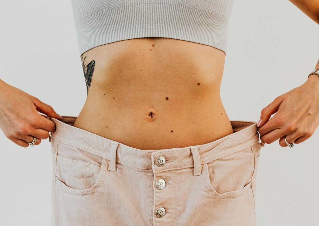 Does Lemon Water Help With Weight Loss? 9 A woman with a stomach tattoo is holding up her pants, showcasing her body art and casual attire.