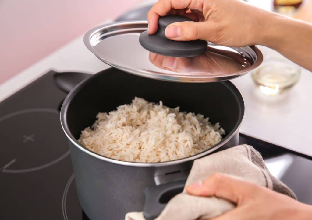 Is Rice Good for Weight Loss? A Nutritionist Explains 5 A pot of freshly cooked white rice on a stovetop, with one hand lifting the lid and another holding a cloth near the pot.