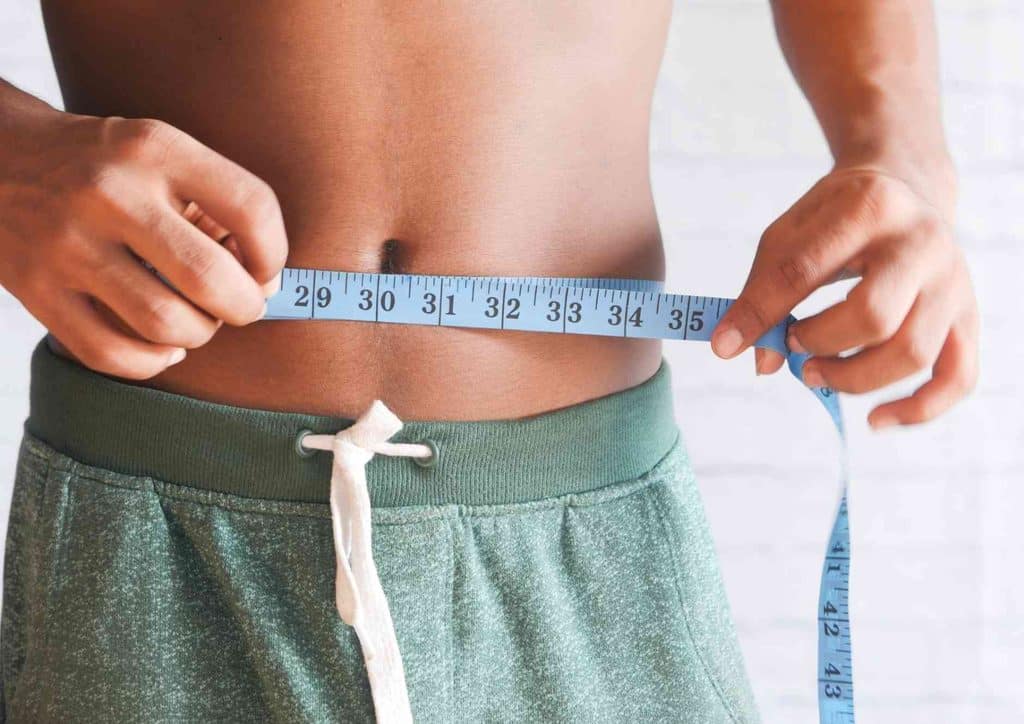 How to Break a Weight Loss Plateau, a Nutritionist's Approach 30 A man measures his waist with a tape measure, focusing on his midsection for fitness tracking.