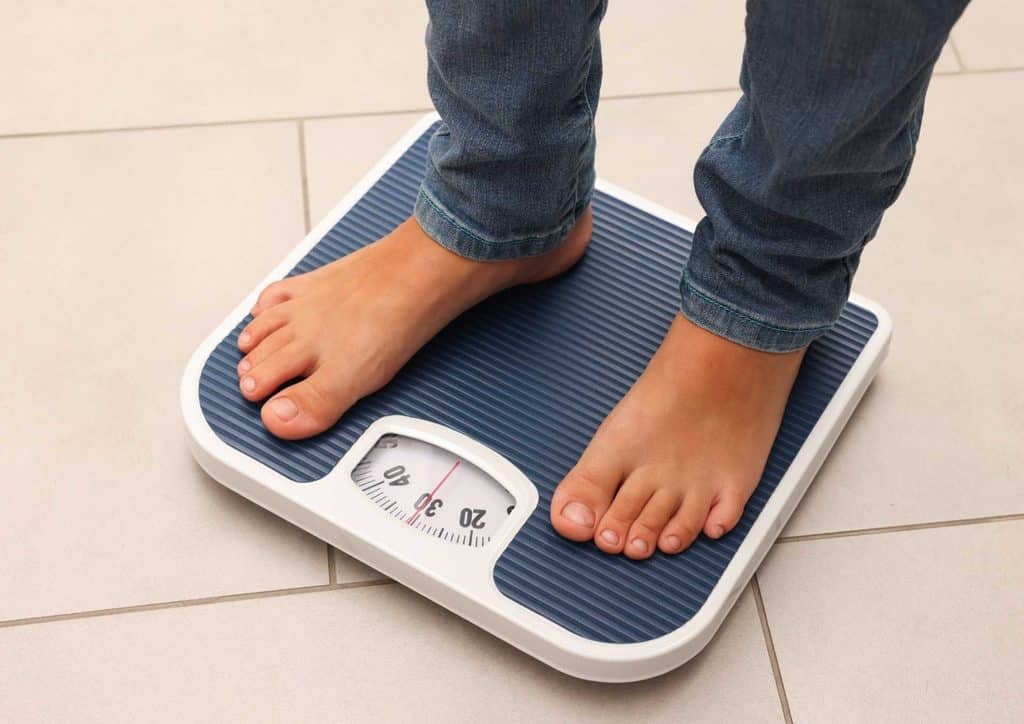How to Break a Weight Loss Plateau, a Nutritionist's Approach 5 A person stands on a scale, feet positioned on the platform, measuring their weight.