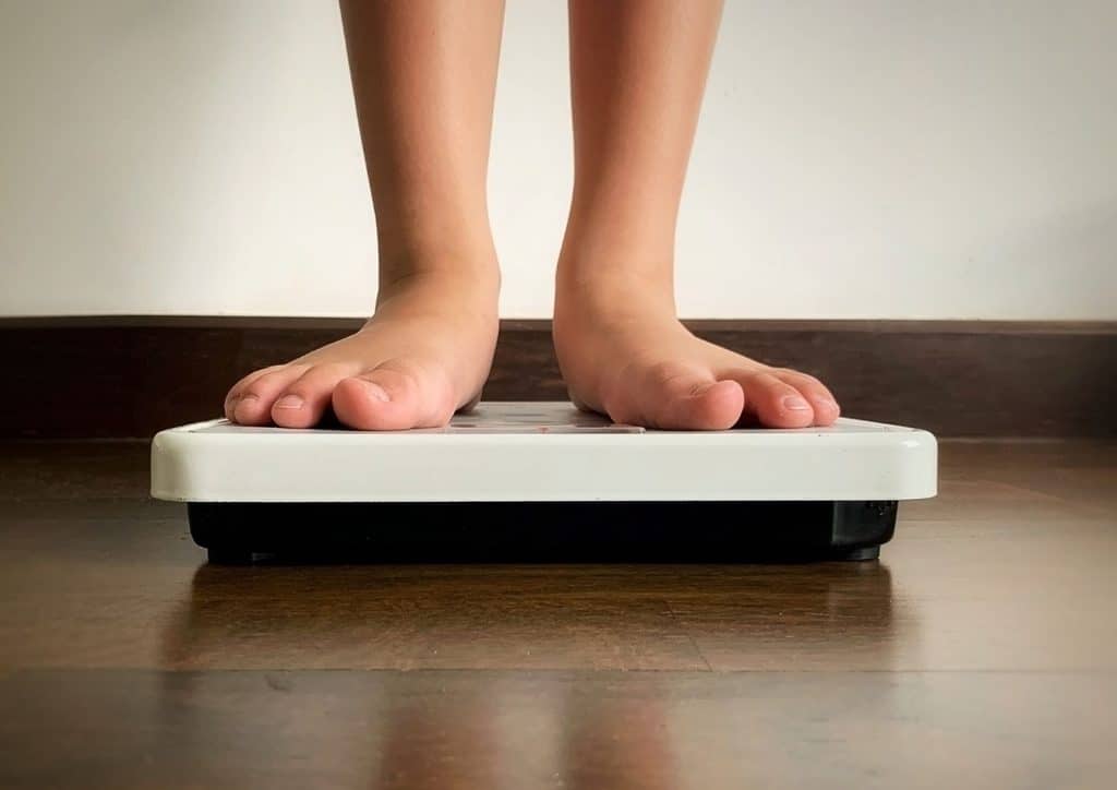 How to Break a Weight Loss Plateau, a Nutritionist's Approach 28 A person stands on a scale, their feet visible, measuring their weight.