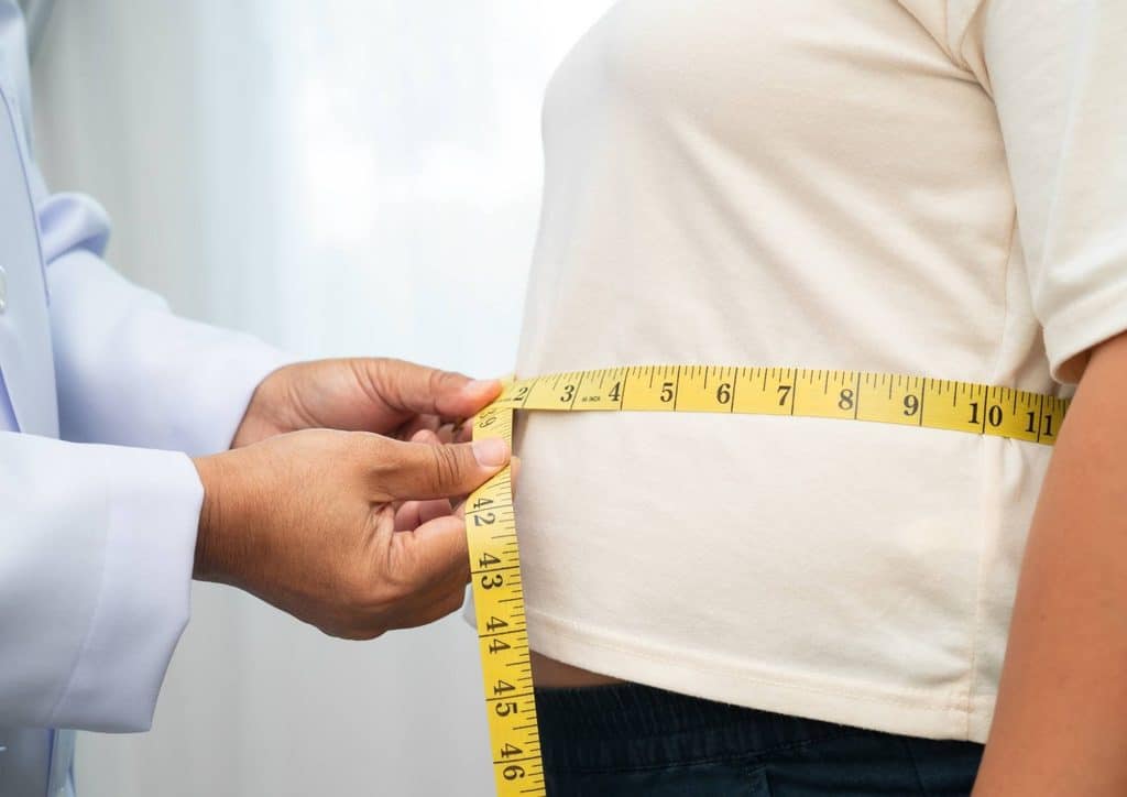 Do Saunas Help With Weight Loss? What Actually Happens 18 A doctor measures the waist of a woman using a measuring tape in a clinical setting.
