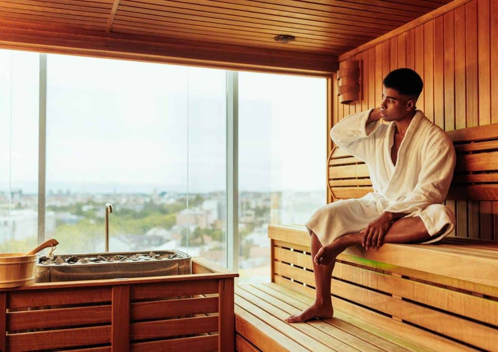 Do Saunas Help With Weight Loss? What Actually Happens 19 A man relaxes in a sauna, enjoying a panoramic view of the city skyline through a large window.