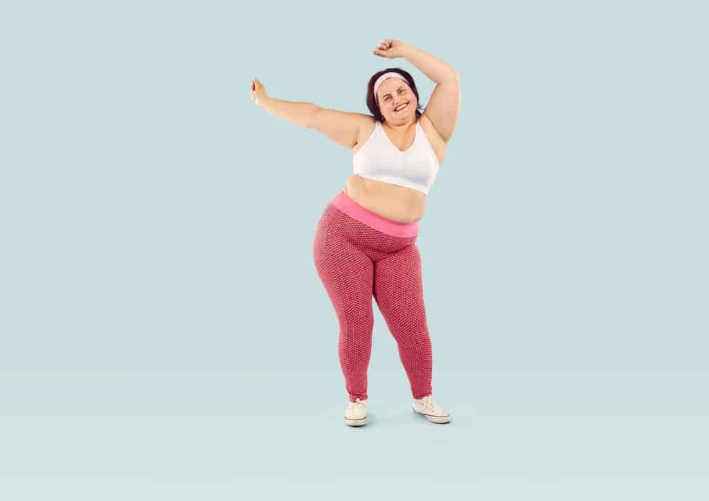 Do Saunas Help With Weight Loss? What Actually Happens 20 A woman in pink pants and a white top is joyfully dancing, showcasing her movement and expression.