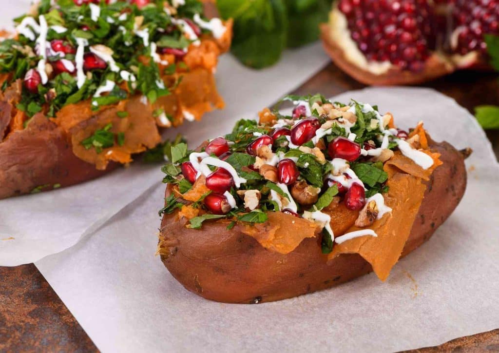 Is Sweet Potato Good for Weight Loss? 20 Two stuffed sweet potatoes topped with pomegranate seeds and fresh herbs, presented on a white plate.