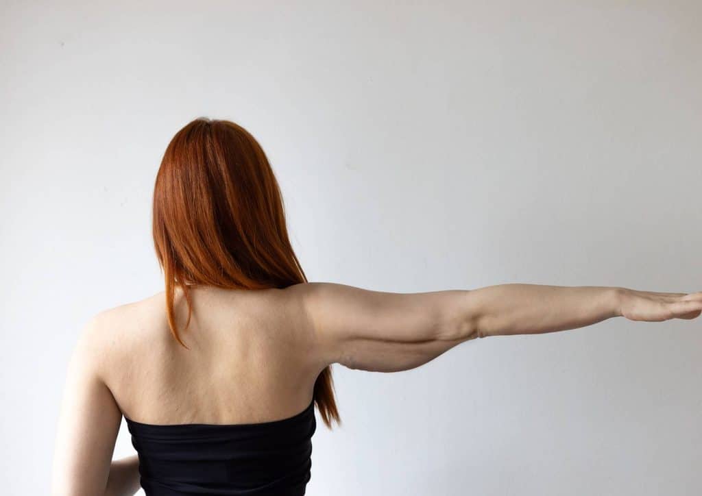 How to Tighten Skin After Weight Loss Naturally 10 A woman with long red hair stretches her arm, showcasing flexibility and grace in a serene environment.