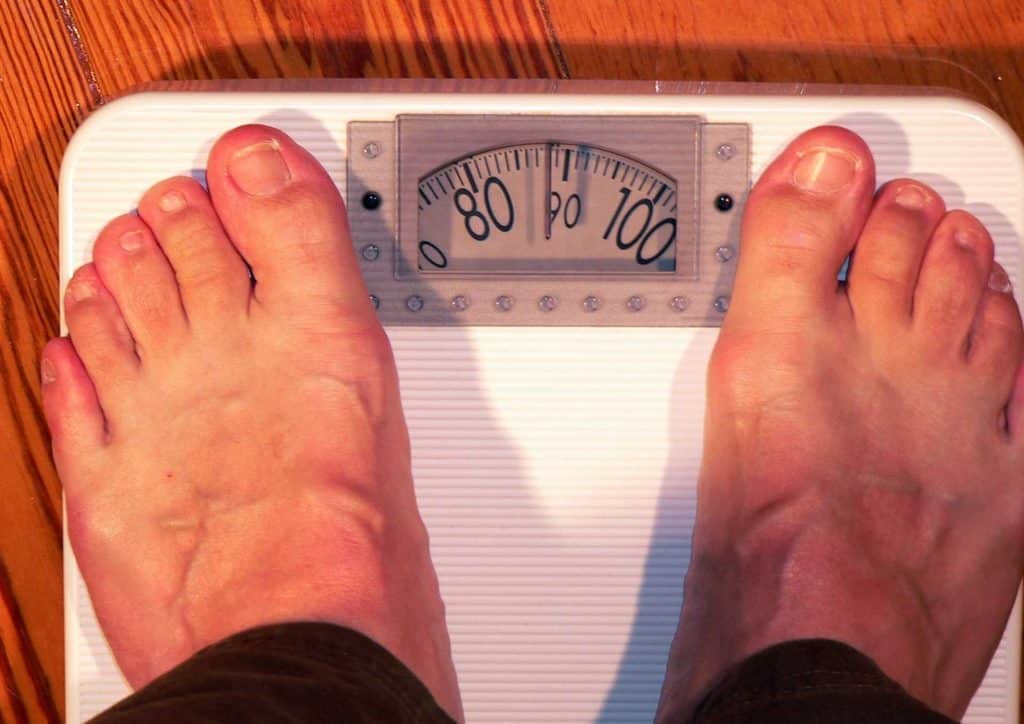 How to Break a Weight Loss Plateau, a Nutritionist's Approach 25 A person stands on a scale, feet positioned on the top, measuring their weight.