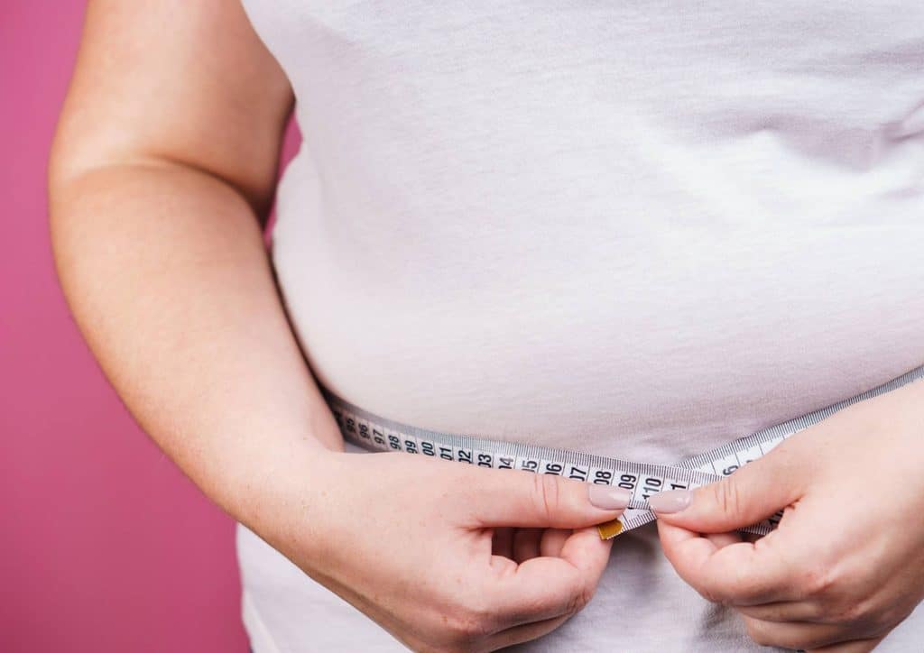 How to Break a Weight Loss Plateau, a Nutritionist's Approach 24 A woman measuring her waist with a tape measure, focusing on her midsection for fitness or health assessment.