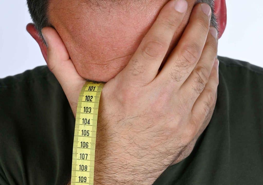 How to Break a Weight Loss Plateau, a Nutritionist's Approach 23 A man is holding his head with his hands, covering his face, expressing distress or frustration.