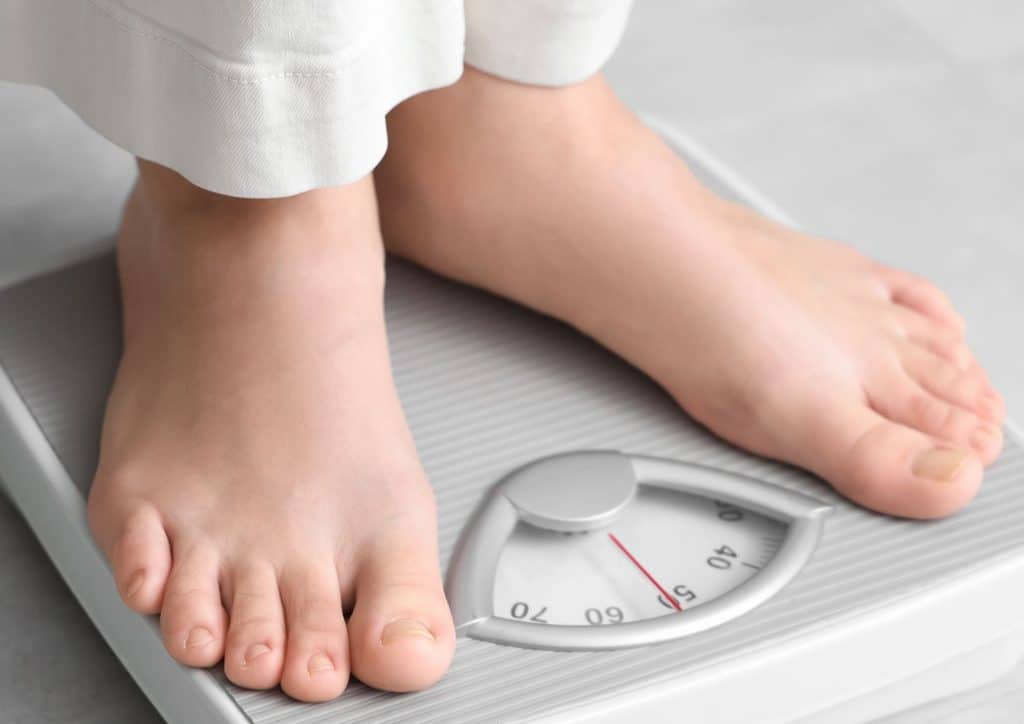 How to Break a Weight Loss Plateau, a Nutritionist's Approach 20 A person stands on a scale, feet positioned on the platform, measuring their weight.
