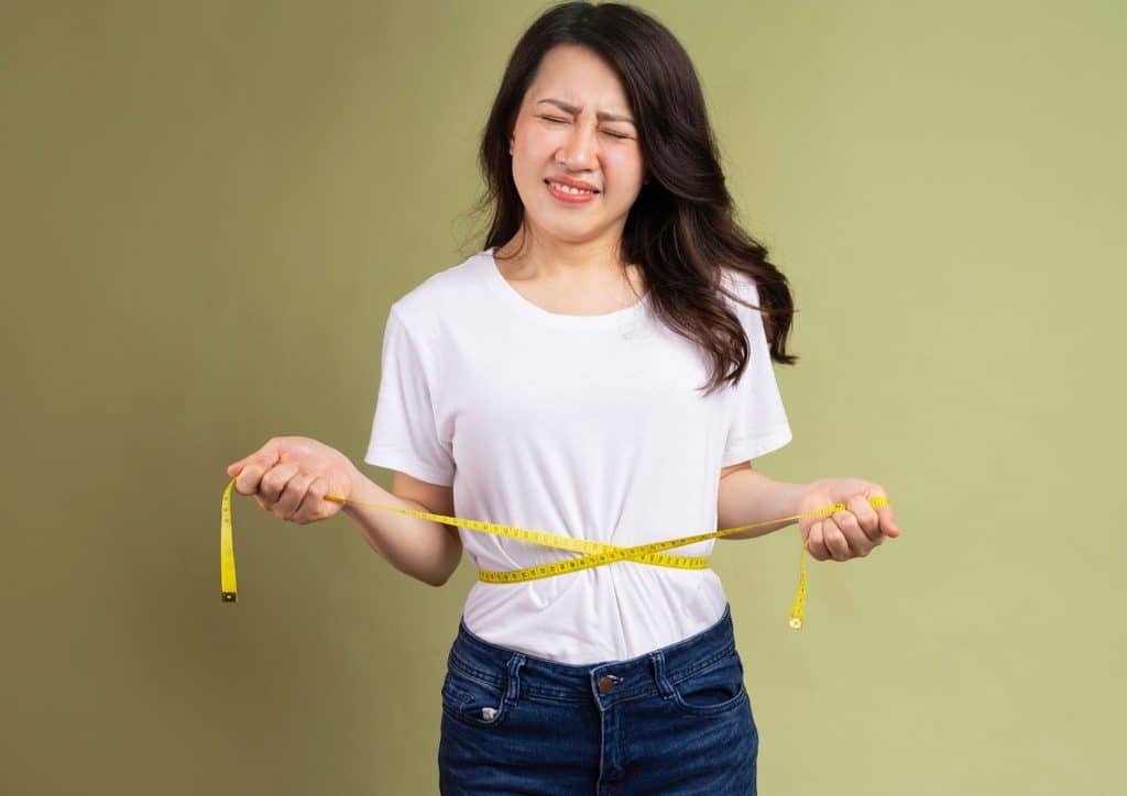How to Break a Weight Loss Plateau, a Nutritionist's Approach 9 A woman holds a yellow tape measure, measuring an object with a focused expression.