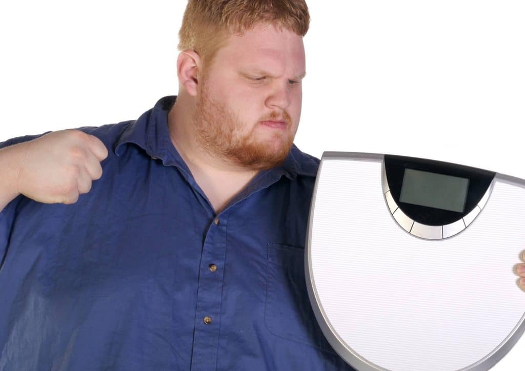 How to Break a Weight Loss Plateau, a Nutritionist's Approach 7 A man stands holding a weight scale, demonstrating its use for measuring weight.