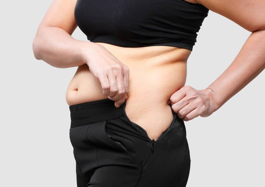 How to Break a Weight Loss Plateau, a Nutritionist's Approach 6 A woman stands with her pants lowered, revealing her stomach in a casual setting.