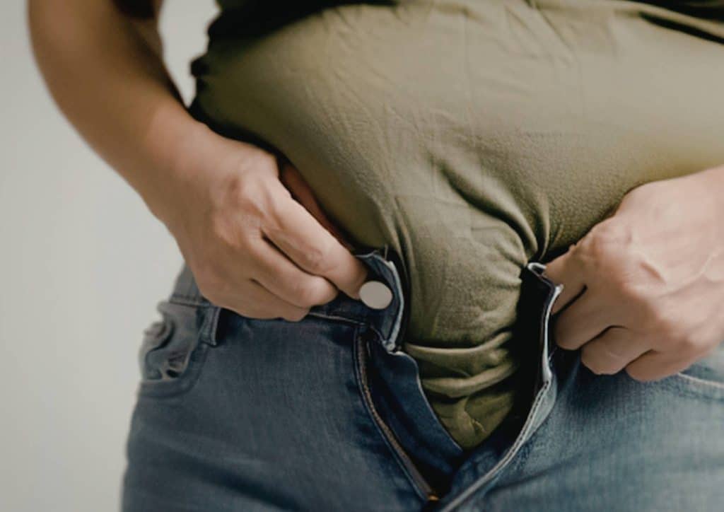 How to Break a Weight Loss Plateau, a Nutritionist's Approach 4 Pregnant woman in jeans gently cradles her belly, showcasing her baby bump with a serene expression.