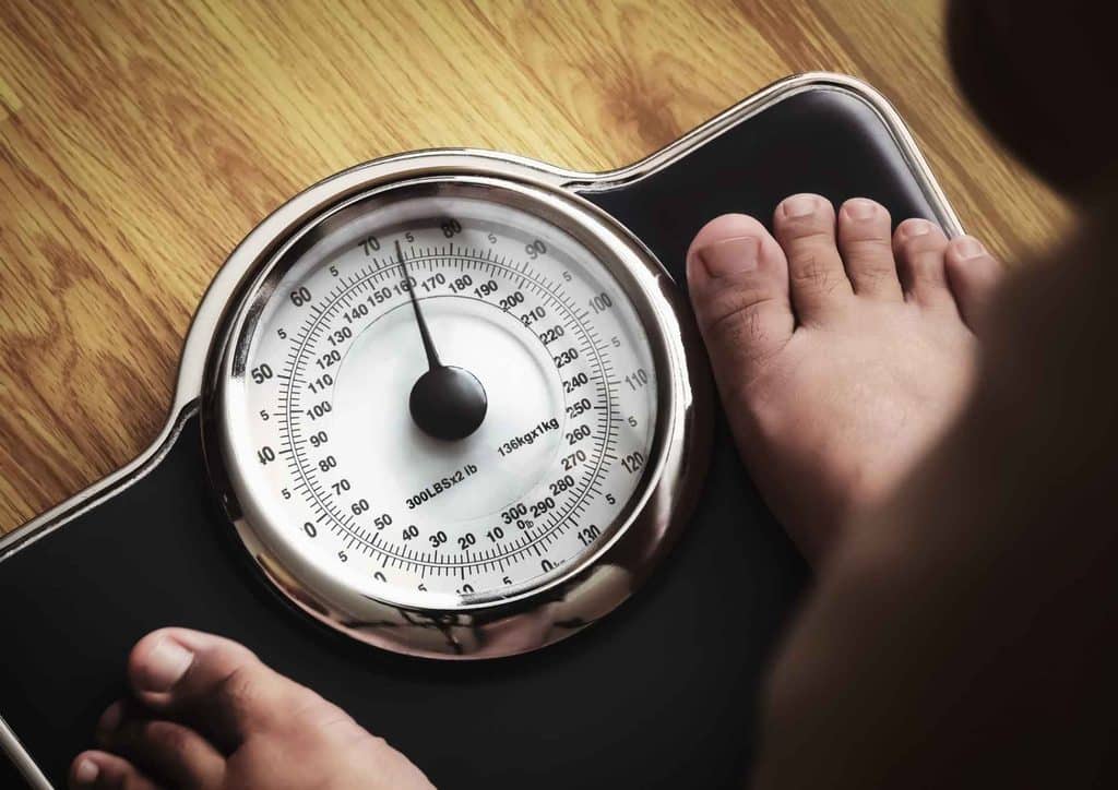 How to Break a Weight Loss Plateau, a Nutritionist's Approach 2 A person stands on a scale, their feet visible, measuring their weight.