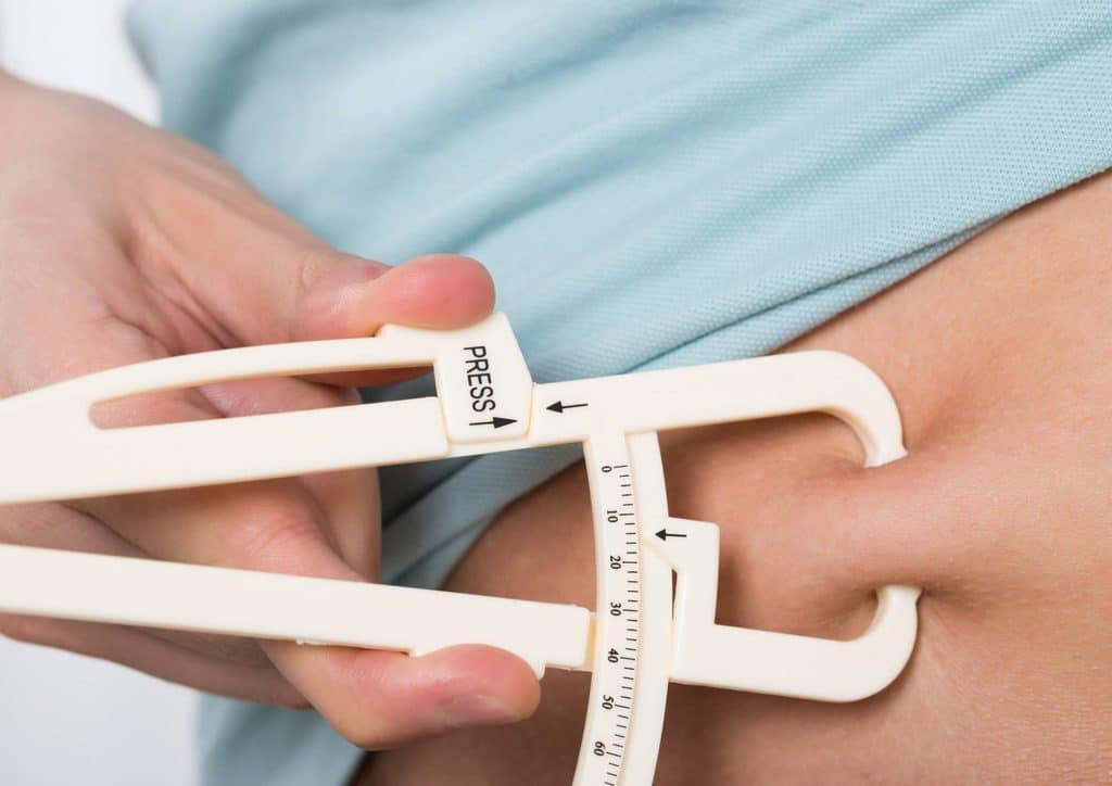 Do Saunas Help With Weight Loss? What Actually Happens 21 A person holds a measuring tape against their stomach, indicating a measurement or assessment of waist size.
