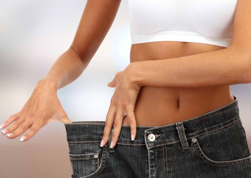 Is Sweet Potato Good for Weight Loss? 5 A woman in a white top and jeans stands with her hands on her waist, smiling confidently at the camera.