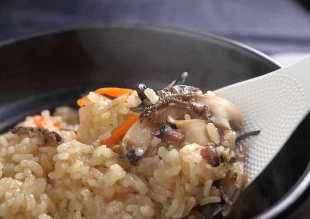 Is Rice Good for Weight Loss? A Nutritionist Explains 7 A close‑up of mixed seasoned rice being scooped with a white rice paddle, containing visible pieces of mushroom, carrot strips, and other vegetables.