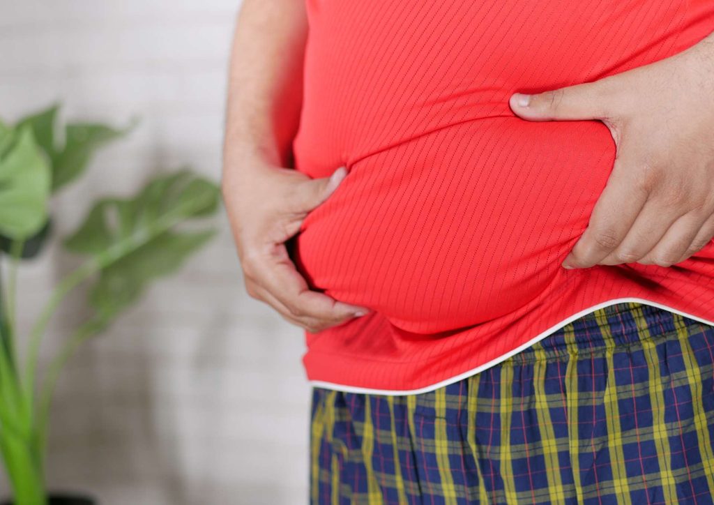 How to Lose Belly Fat: What a Nutritionist Recommends 2 A man in red shorts measures an object with a tape measure, focusing intently on the measurement.