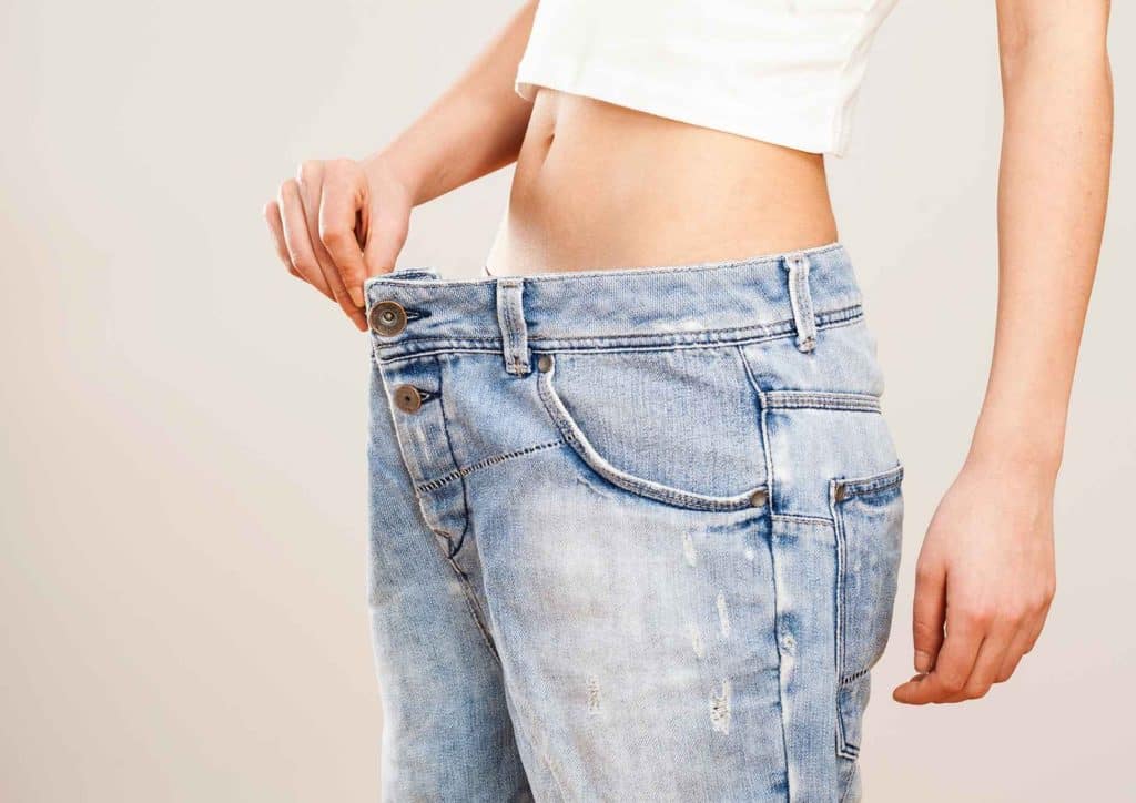 How to Lose Belly Fat: What a Nutritionist Recommends 3 A woman in jeans stands with her hands on her waist, looking confidently at the camera.