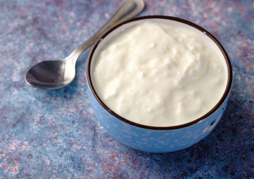The Best Foods for Weight Loss 7 Yoghurt in a blue bowl with a spoon, set against a matching blue background.