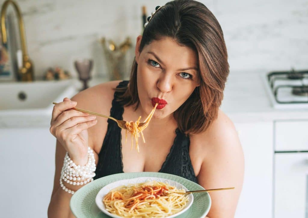 Is Pasta Good for Weight Loss? 6 A woman enjoying a plate of spaghetti, twirling pasta with a fork, seated at a dining table.