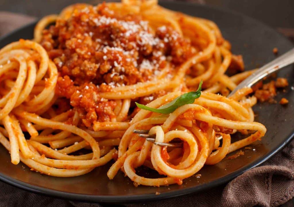Is Pasta Good for Weight Loss? 9 A black plate holds a serving of spaghetti topped with rich meat sauce, garnished with herbs.