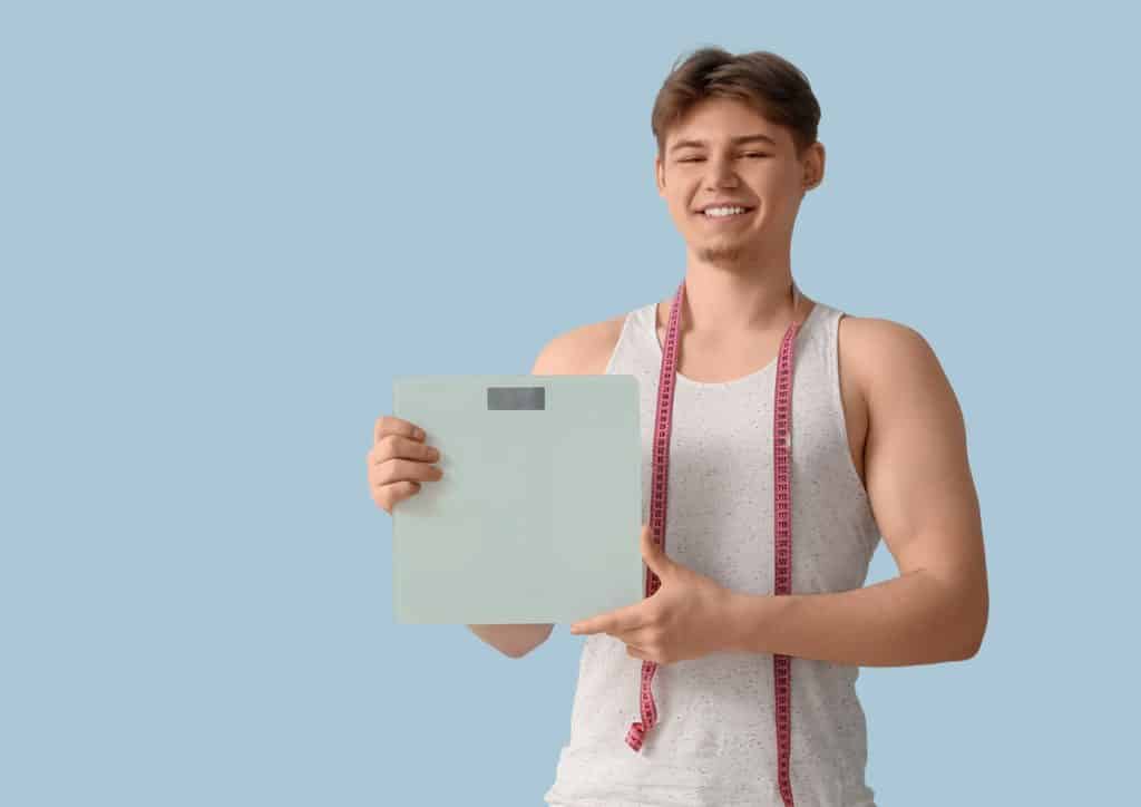 Is Pasta Good for Weight Loss? 3 A man holds a scale in one hand and a measuring tape in the other, demonstrating measurement tools for weight and dimensions.