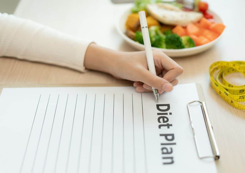How to Lose Belly Fat: What a Nutritionist Recommends 7 A diet plan on paper alongside various food items and a measuring tape, illustrating a healthy eating strategy.