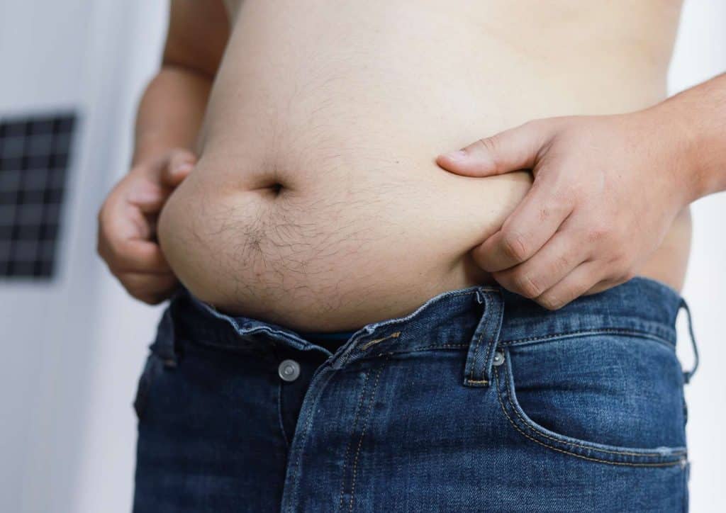How to Lose Belly Fat: What a Nutritionist Recommends 5 A man with a prominent belly wearing blue jeans, standing casually with a neutral expression.