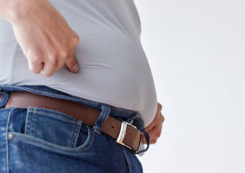 How to Lose Belly Fat: What a Nutritionist Recommends 13 A man wearing a belt, with his hand resting on his belly, appears thoughtful and relaxed.