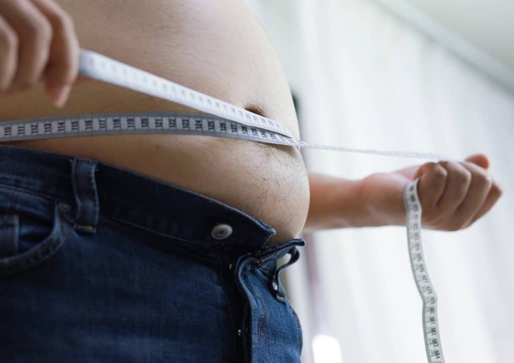 How to Lose Belly Fat: What a Nutritionist Recommends 15 A man measuring his waist with a measuring tape, focusing on his midsection for accurate sizing.