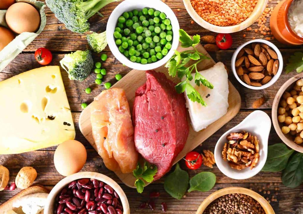 High-Protein Foods for Weight Loss 14 A diverse assortment of foods featuring meat, vegetables, nuts, and eggs arranged on a wooden table.