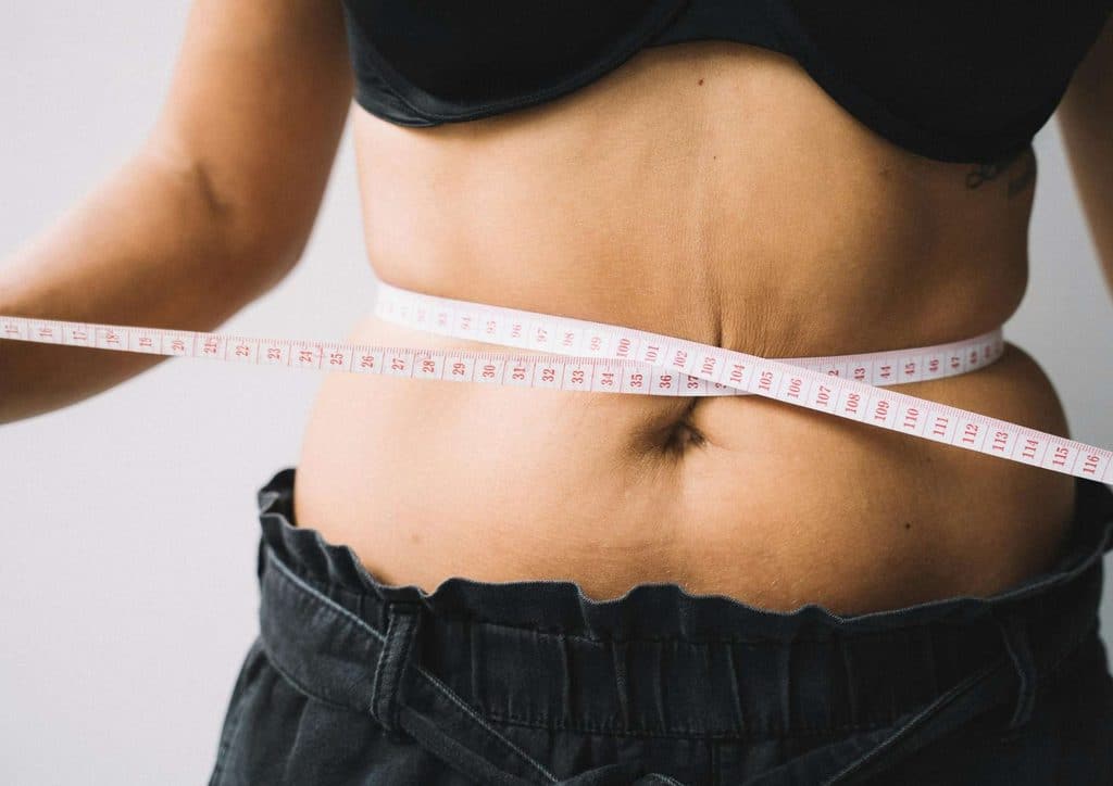Is Pasta Good for Weight Loss? 19 A woman measuring her waist with a tape measure, focusing on her midsection in a well-lit room.