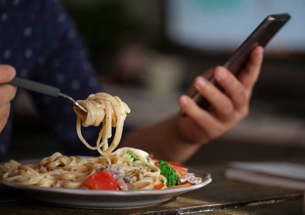 Is Pasta Good for Weight Loss? 28 A person enjoying a plate of pasta while holding a cell phone in their other hand.