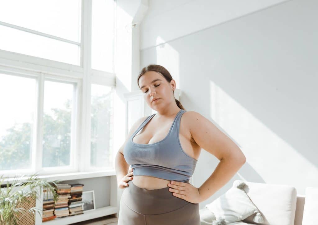 How to Lose Belly Fat: What a Nutritionist Recommends 4 A woman in a sports bra stands confidently in a well-lit room, showcasing her athletic physique.