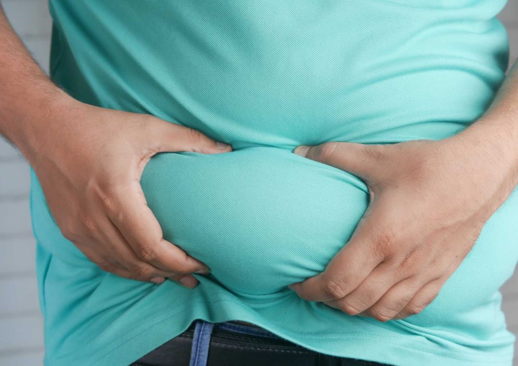How to Lose Belly Fat: What a Nutritionist Recommends 30 A man stands with his hands on his stomach, indicating discomfort or pain.