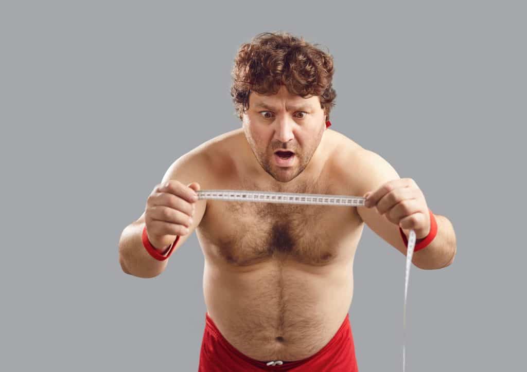 How to Lose Belly Fat: What a Nutritionist Recommends 1 A man in red shorts measures an object with a tape measure, focusing intently on the measurement.