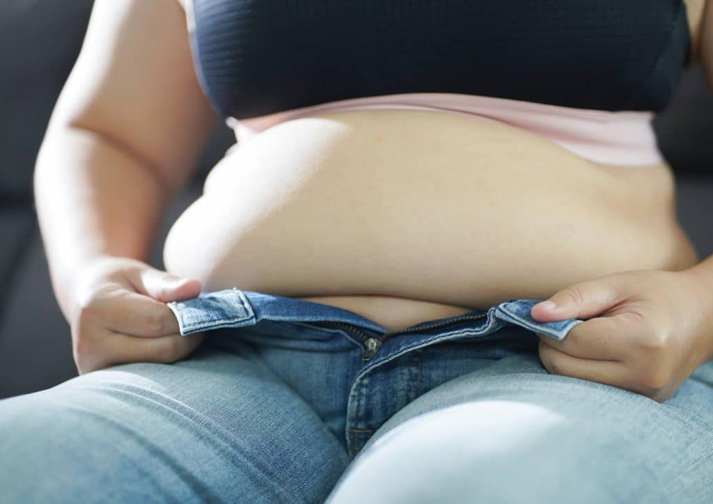 How to Lose Belly Fat: What a Nutritionist Recommends 10 A woman in jeans gently holds her belly, conveying a sense of comfort or contemplation.
