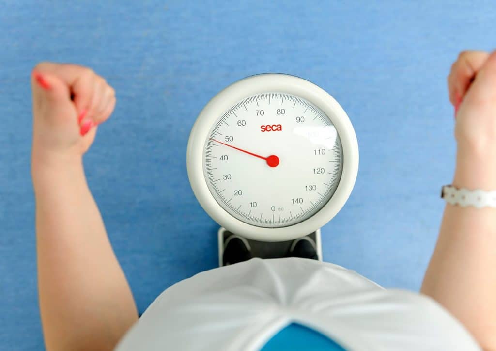 How to Lose Belly Fat: What a Nutritionist Recommends 16 A person stands on a scale with arms raised, indicating a moment of measurement or celebration.