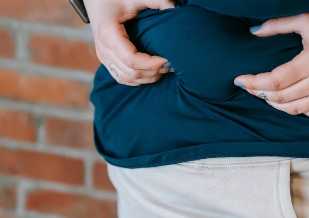 How to Lose Belly Fat: What a Nutritionist Recommends 18 A woman gently holds her stomach with both hands, expressing a sense of discomfort or concern.