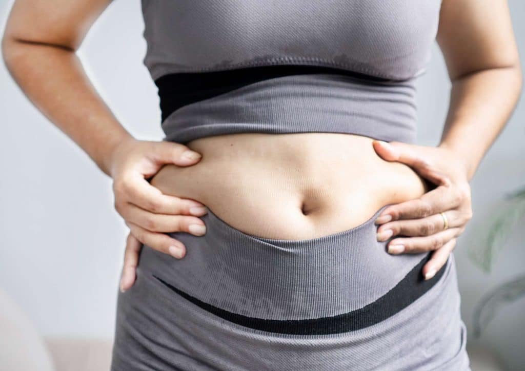 How to Lose Belly Fat: What a Nutritionist Recommends 23 A woman confidently displays her bare stomach, showcasing her belly in a casual setting.