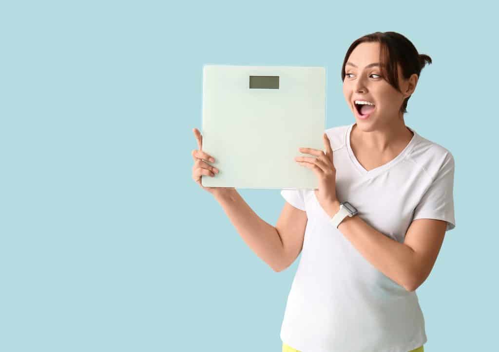 How to Lose Belly Fat: What a Nutritionist Recommends 29 A surprised woman holds a weight scale, expressing shock at the reading displayed on it.