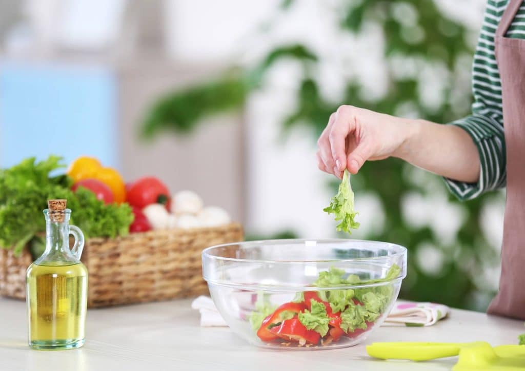 The Best Foods for Weight Loss 14 A woman is chopping fresh vegetables to prepare a colorful salad in a bright kitchen.