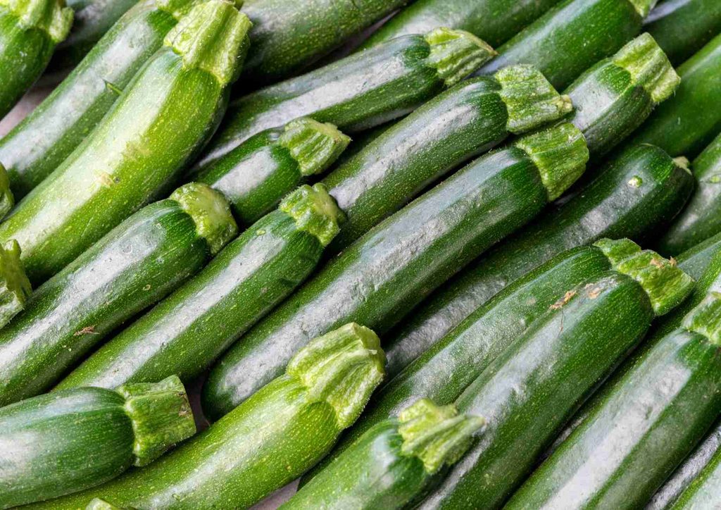 The Best Foods for Weight Loss 27 Close-up of fresh zucchini on a white surface, showcasing its smooth skin and vibrant green colour.