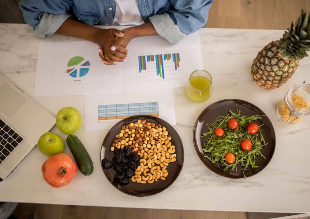 Nutritionist vs Clinical Nutritionist: What's the Difference? 5 A woman sits at a table with a laptop, accompanied by two plates of food in front of her.