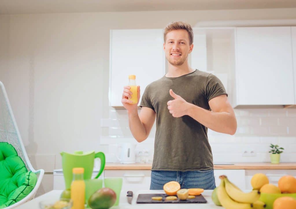 Clinical Nutritionist vs Nutritionist: What's the Difference 19 Smiling man in a kitchen holding a glass of juice, conveying a sense of enjoyment and warmth.