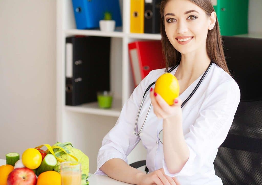 Clinical Nutritionist vs Nutritionist: What's the Difference 15 A woman in a white coat holds an orange, smiling as she looks at the fruit in her hand.