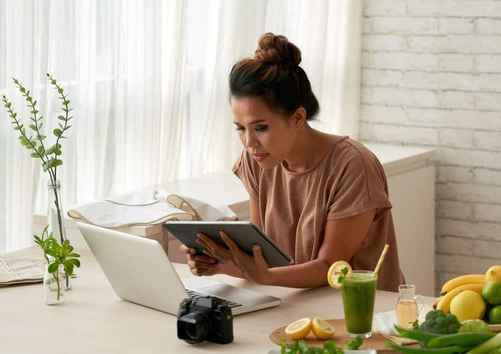 Clinical Nutritionist vs Nutritionist: What's the Difference 10 A woman seated at a table, working on a laptop with a glass of juice beside her.